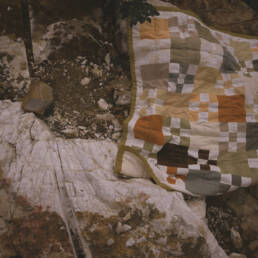 A naturally dyed quilt by Chelsea Smith lies out on the ground across large rocks, 2023.