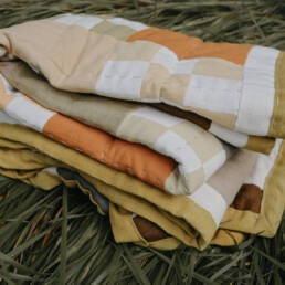 A naturally dyed quilt by Chelsea Smith sits folded on top of tall folded over grass, 2023.