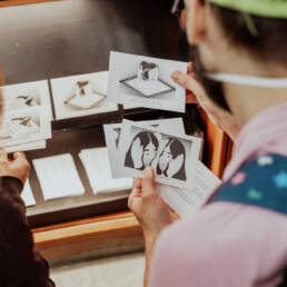 A view over the shoulders of two people who are looking at index-sized cards as part of Myung-Sun Kim’s exhibition Rituals for Belonging at Toronto Public Library – Lillian H. Smith Branch, 2023.