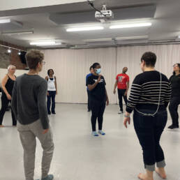 Nine people stand in a circle around a masked instructor at Kevin Ormsby’s Showcase Workshop, 2023.