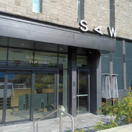The front of SAW in Ottawa with white vinyl writing by Juliane Foronda above the door that reads as “Words within words are permissible,” 2023.